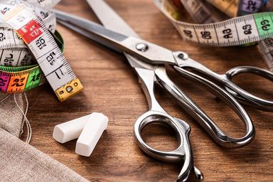 Primer plano de tijeras, cintas métricas y tiza de sastre sobre una mesa de madera